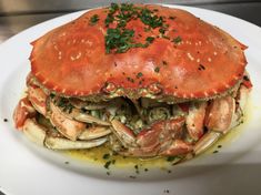 a large crab on a white plate with sauce and parsley sprinkled on top