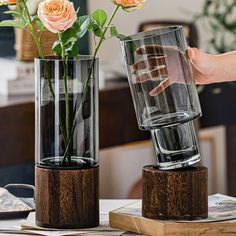 two vases that have flowers in them on top of a wooden table with glasses