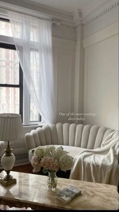 a living room filled with white furniture and flowers on top of a wooden coffee table