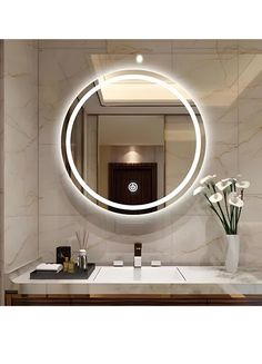 a bathroom sink with a round mirror above it and flowers in front of the counter