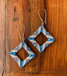 two square shaped beaded earrings sitting on top of a wooden table