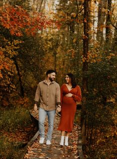 a man and woman standing on a wooden walkway in the woods with leaves all around them