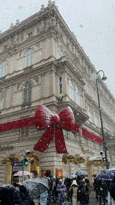 people are walking in the rain with umbrellas and bows on their head as they walk past a large building