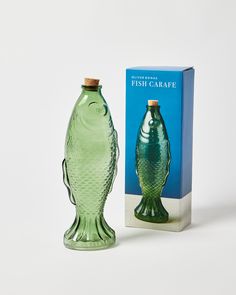 a green glass fish shaped bottle next to a box