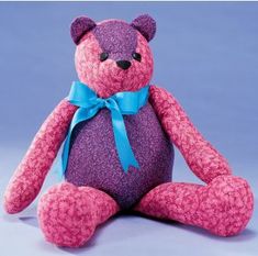 a pink and purple teddy bear with a blue ribbon on it's neck sitting in front of a blue background