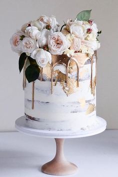 a white and gold cake with flowers on top sitting on a table next to a wall