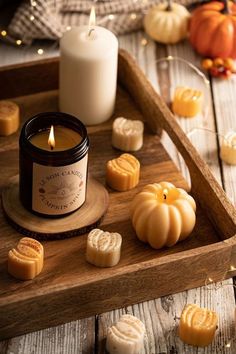 a candle and some cookies on a wooden tray with pumpkins in the foreground