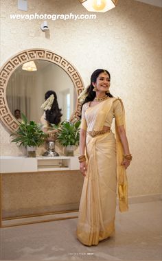 a woman standing in front of a mirror wearing a yellow sari and gold jewelry