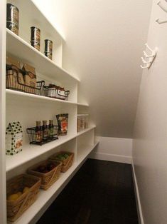 a pantry with white shelving and lots of food in baskets on the bottom shelf