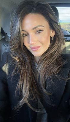 a woman sitting in the back seat of a car with long hair and brown eyes