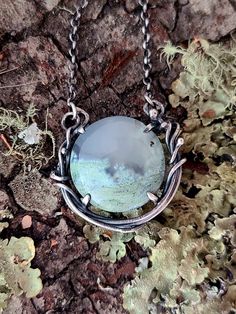 A round moss agate is wreathed in a tangle of silver vines. The translucent agate has bright green inclusions growing at the bottom half of the stone, like soft mosses trapped in ice. The stone sits in a silver frame with four prongs holding it in place. The silver has been oxidized and given a brushed finish to highlight the textures. Made by hand from sterling silver, the pendant measures 1 1/4" long and 1 1/4" wide. The fine oval rolo chain adjusts from 20" to 24" in length. This one of a kind necklace is ready to ship! Metalwork Jewelry, Rustic Jewelry, Rolo Chain, Moss Agate, Silver Frame, Bright Green, Earring Necklace, Ring Necklace, Tangled