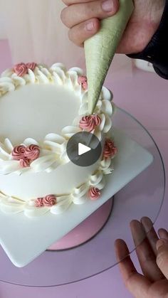 a person is cutting into a cake with white frosting and pink roses on it