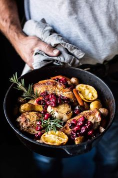 a person holding a skillet filled with chicken and cranberries