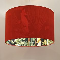 a red lampshade hanging from a ceiling in a room with plants and birds on it