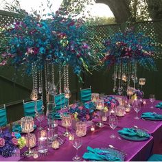 the table is set up with purple and blue flowers in vases, teal napkins, and candles