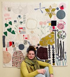 a woman sitting in front of a quilted wall hanging on the side of a wall