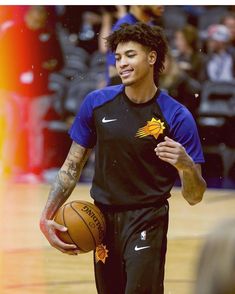 a man holding a basketball in his right hand and walking on a court with other people watching