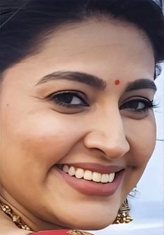 a close up of a woman smiling and wearing a red necklace with gold jewelry on it