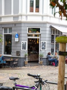 people are sitting at tables in front of a restaurant with bicycles parked outside the building