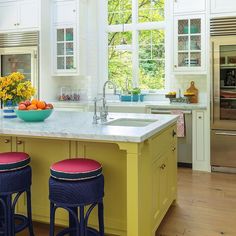 two blue stools sit in front of a kitchen island with yellow cabinets and white countertops