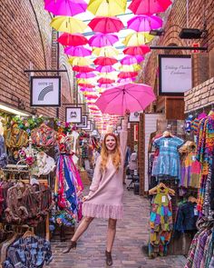 a woman is standing under an umbrella in the middle of a market area with other items on display