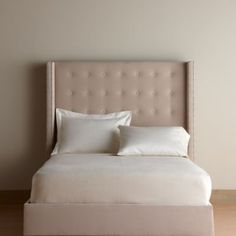 a white bed with two pillows on top of it and a beige headboard in the background