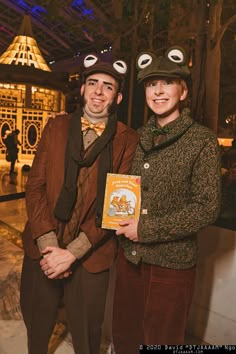 two people dressed in costumes standing next to each other holding a book with googly eyes on them