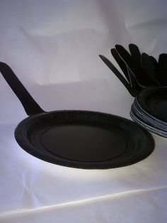 two black paper plates with forks and knives in them on a white tablecloth background