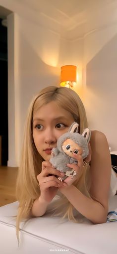 a woman laying on top of a white bed holding a stuffed animal next to her face