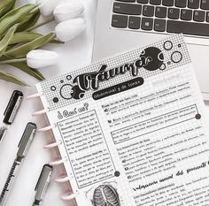 an open notebook sitting on top of a desk next to a laptop computer and flowers