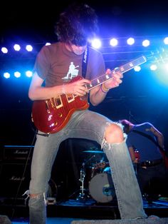 a young man playing guitar on stage at a music concert with lights in the background