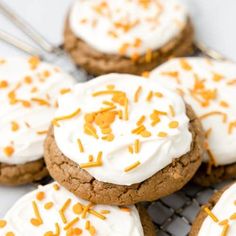 cookies with white frosting and orange sprinkles are cooling on a wire rack