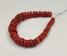 a red beaded necklace is displayed on a white surface with a metal hook in the middle