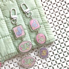 three charms with letters on them sitting next to a green piece of cloth and pink fabric