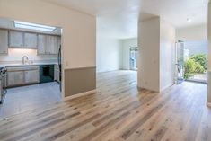 an empty kitchen and living room in a house with wood floors, white walls and cabinets