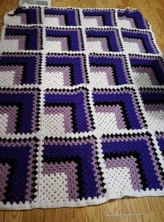 a purple and white crocheted blanket sitting on top of a wooden floor