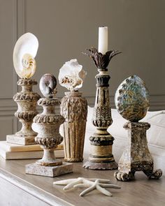 an assortment of vases and candles on a table in front of a white couch