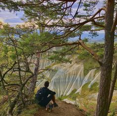 a man sitting on top of a hill next to trees