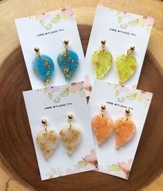 four different colored heart shaped earrings on top of a wooden table next to a card