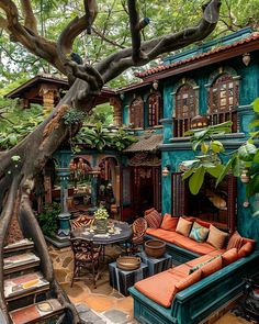 an outdoor living area with couches, tables and chairs under a tree in front of a house