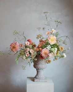 a vase filled with lots of flowers sitting on top of a white pedestal next to a wall