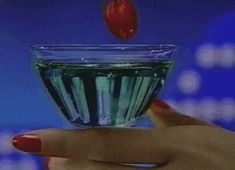 a woman's hand holding a cup with liquid in it and a strawberry floating out of it