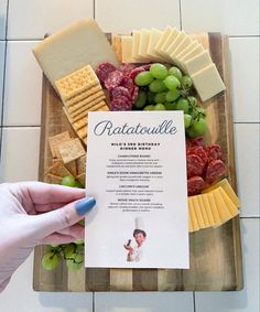 a person holding up a card with cheese, grapes and crackers next to it