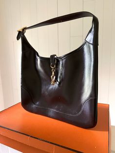 This vintage Hermès Trim 31 Hobo Bag is crafted from luxurious chocolate brown Box leather and is accented with gold-tone hardware. Featuring an adjustable shoulder strap, trim closure at front and gusseted sides. Unlined interior. Includes box and extra strap. Measuring: 11.25 in. L, 9 in. H, .25 in. D. Very good condition. Luxurious Chocolate, Vintage Hermes, Brown Box, Dior Shoes, Chanel Handbags, Hobo Bag, Chocolate Brown, Shoulder Strap, Dior