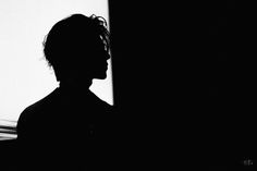 a person standing in the dark with their head turned to the side and his shadow behind him