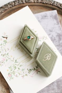 an engagement ring with a green stone sits on top of a card next to it