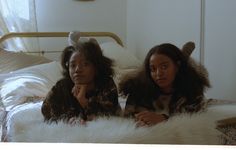 two women sitting on a bed with white fur