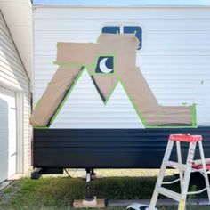 the back of a mobile home with a ladder next to it and a painting on the side of the trailer