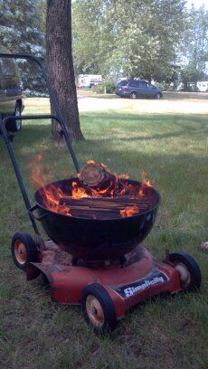 a fire pit sitting in the grass next to a lawn mower with wheels on it