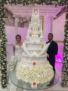 a man and woman standing next to a giant cake with flowers on it's side